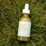 A clear dropper bottle of cloudy and green milky oats extract resting in green grass
