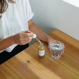 person dispensing fresh milky oats tincture from a dropper bottle into a glass of water