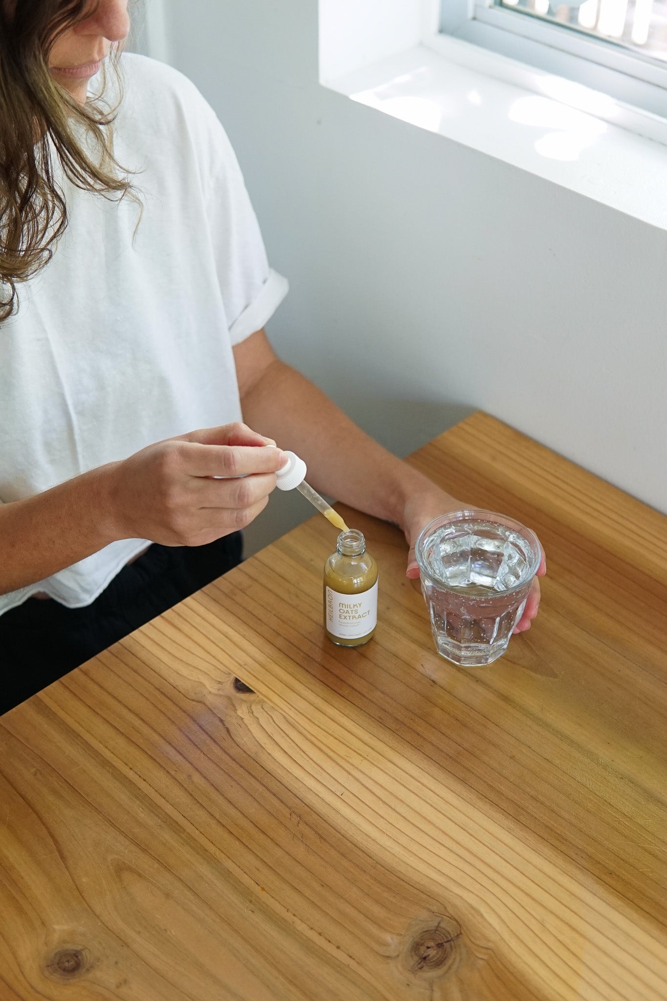 person dispensing fresh milky oats tincture from a dropper bottle into a glass of water